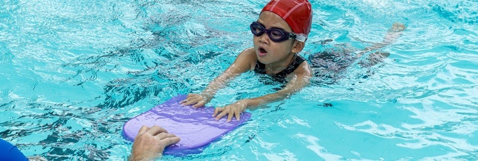 Small child in pool learning to swim with aid of kickboard