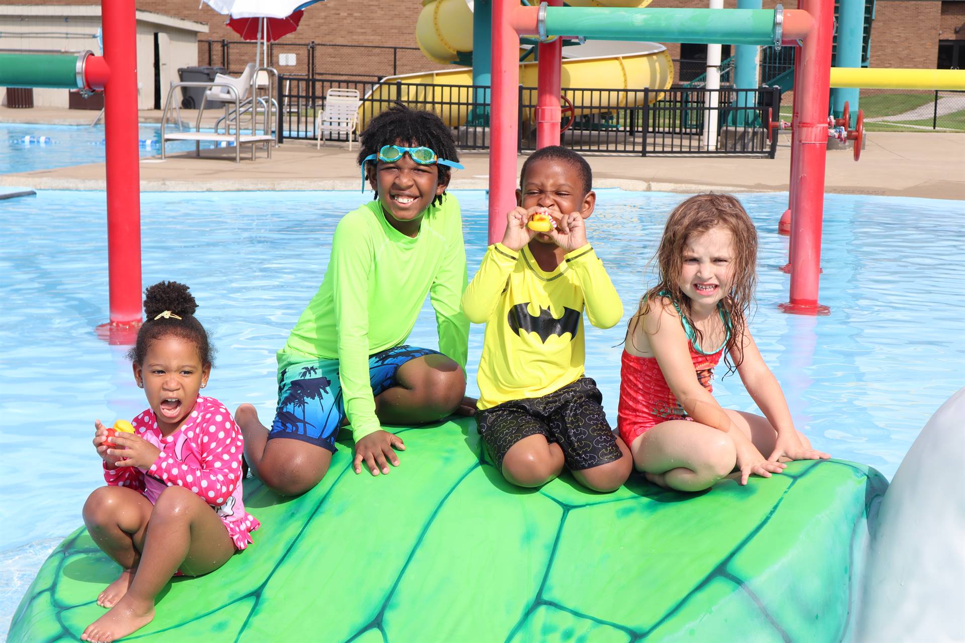 Four children sitting on a turtle water feature at the outdoor pool 