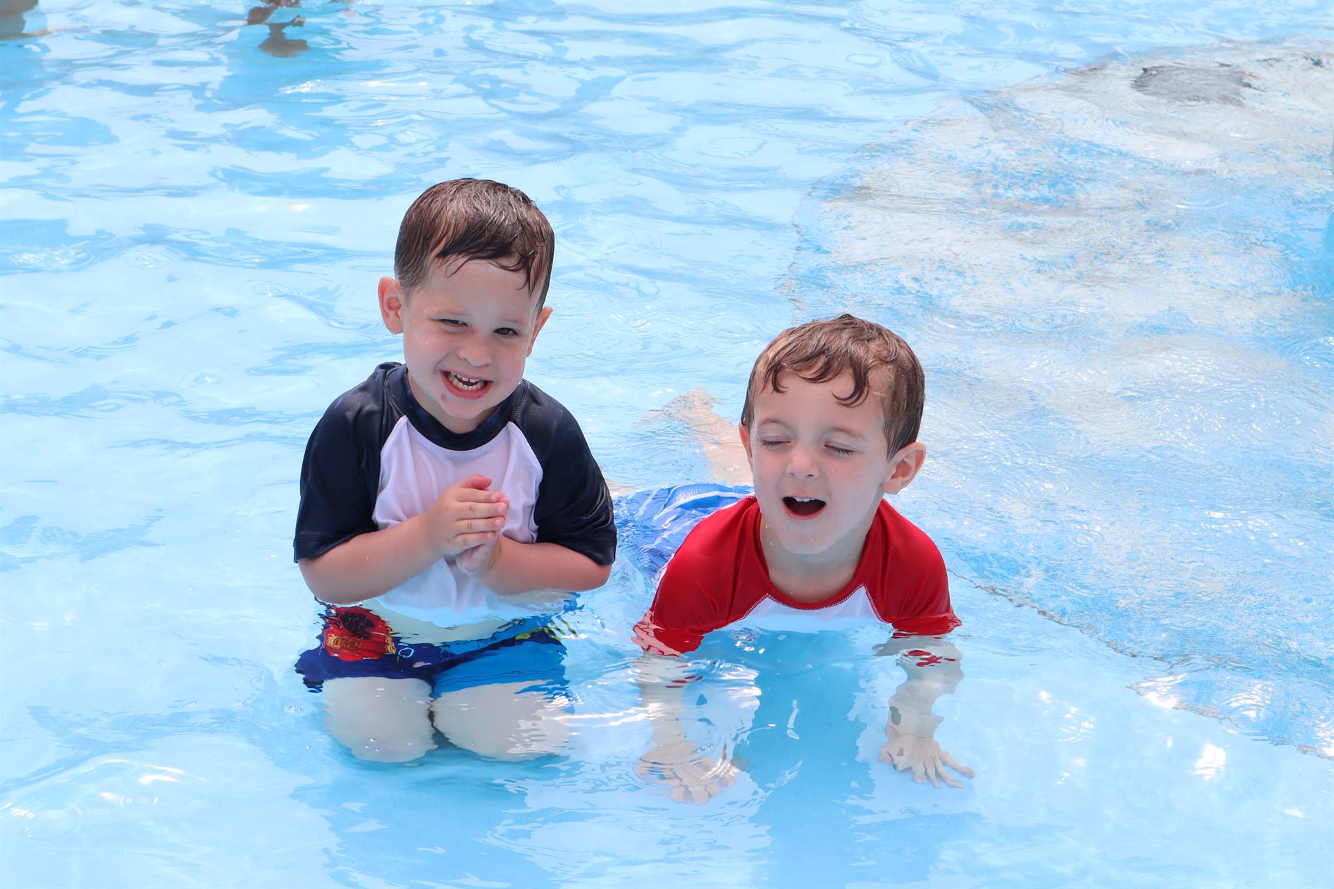 Two children smiling in the splash area of the outdoor pool 