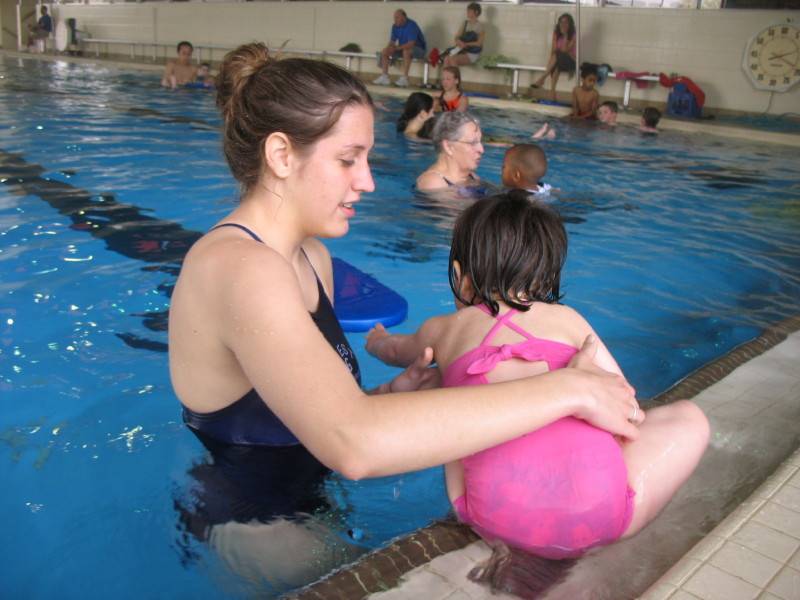 A woman helping a child on the edge of the indoor pool 